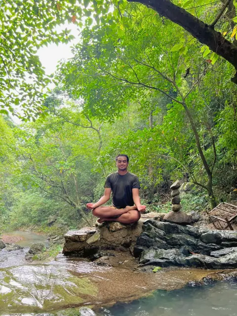 Merald meditating on a rock beside a forest stream