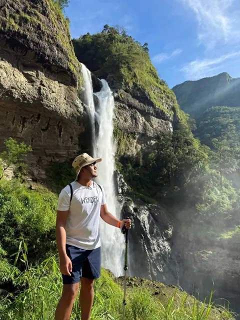 Merald standing beside a tall waterfall