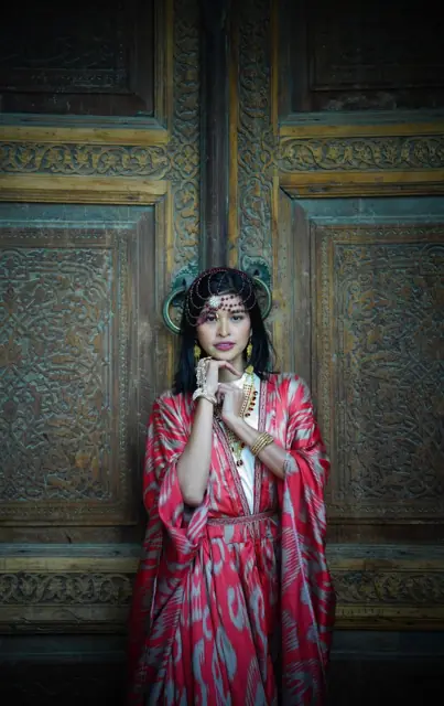 Mirjan in traditional dress in front of an ornate wooden door