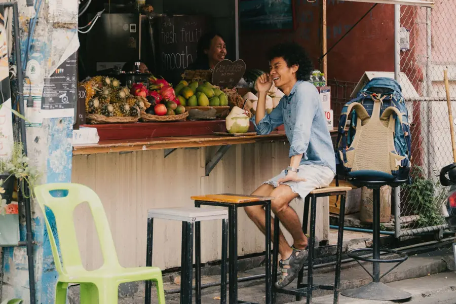 A traveller laughing with the owner of a fresh fruit stall on a street in Thailand
