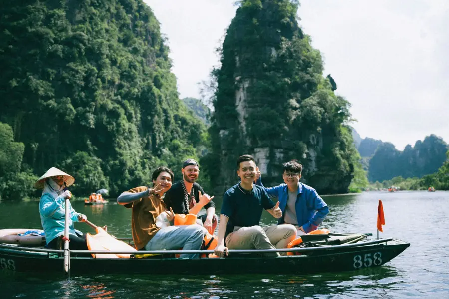 Four travellers smiling in a rowing boat among the limestone karsts of Ninh Binh, Vietnam, with their local rower