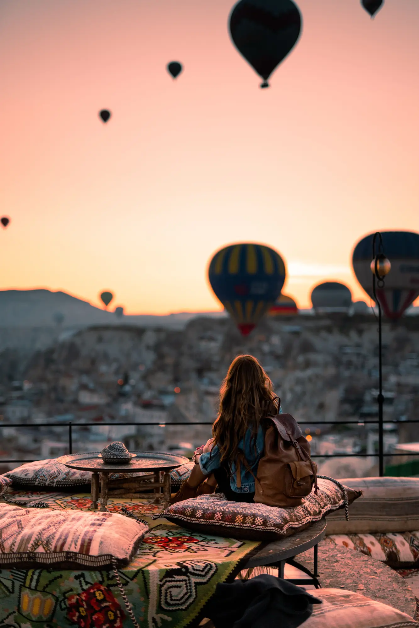 A traveller on a rooftop terrace in Göreme watching hot air balloons rise over Cappadocia, Turkey at sunrise