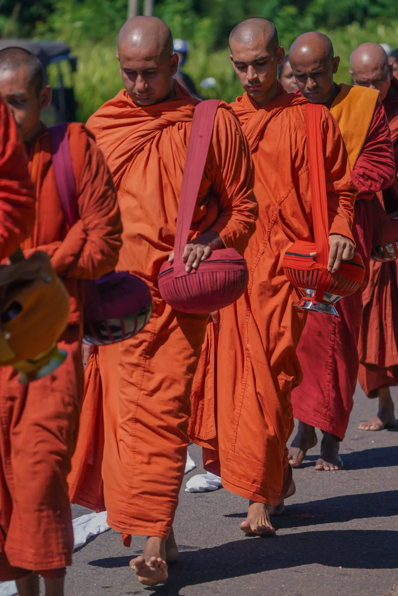 Theravada Buddhist monks in saffron robes walking barefoot with alms bowls in a procession in Sri Lanka
