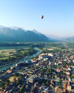 Discover the breathtaking aerial view of Vang Vieng, Laos, with a hot air balloon soaring above the town.